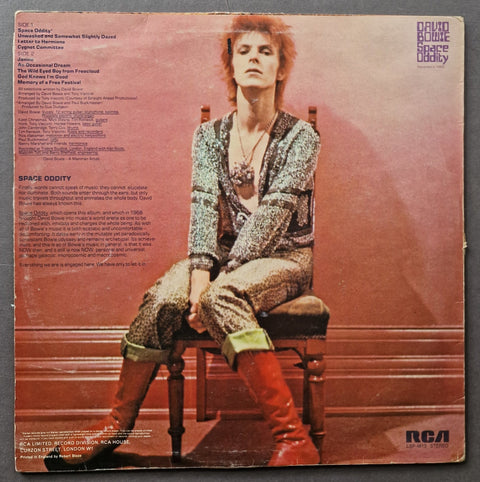 The back cover of a vintage RCA vinyl record for David Bowie's album 'Space Oddity', featuring a large photo of David Bowie seated on a wooden chair against a pinkish background, with tracklist and catalog text on the left and the RCA logo in the bottom right corner.