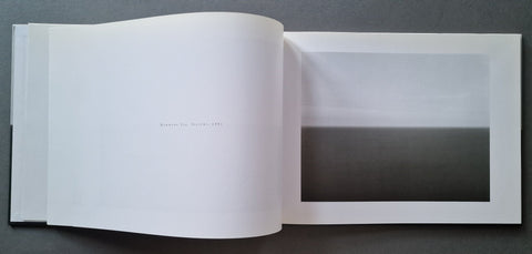 An open art book, showing a minimalist black-and-white landscape photograph printed on one page with a large white margin.
