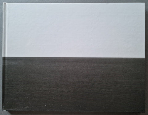 A hardcover book with a two-tone cover design, featuring a white top half and a dark charcoal gray wood-grain textured bottom half, shown against a dark gray background.
