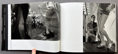 An open black-and-white art book or magazine spread, showing two photographic pages with fashion/editorial imagery. A human hand is visible holding the left edge of the book against a dark background.
