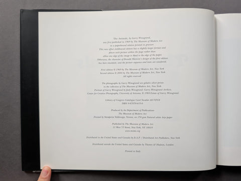 An open hardcover book showing the printed title and copyright page on the left page, photographed from above against a dark gray background. A finger is visible holding the lower left edge of the book.