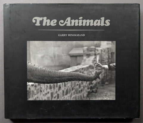 The Animals book by Garry Winogrand, featuring a black cover with white title text and a central black-and-white photograph of an elephant trunk reaching toward a human hand.