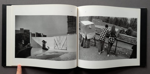 An open black-and-white art book or photo album held open by a hand, showing two printed photographic pages side by side against a dark background.