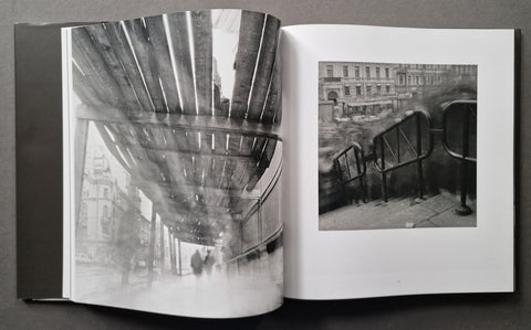 An open book showing two black-and-white architectural photographs on the pages, photographed against a dark gray background.