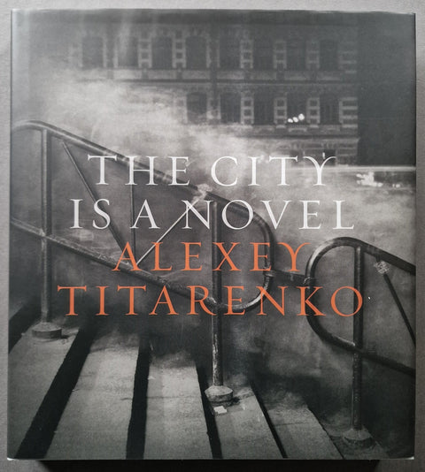 The book cover of 'The City Is A Novel' by Alexey Titarenko, featuring a dark, moody photograph of city stairs and a building with the title in white and orange text.