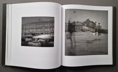 An open book displaying two black-and-white photographic prints side by side on white pages, photographed against a dark gray background.