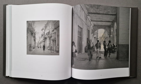 An open book showing two black-and-white photographic prints side by side, photographed against a dark gray background.