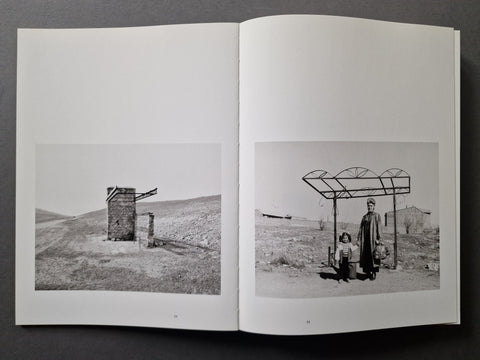 An open book showing two black-and-white photographic prints on the pages, photographed against a dark gray background.