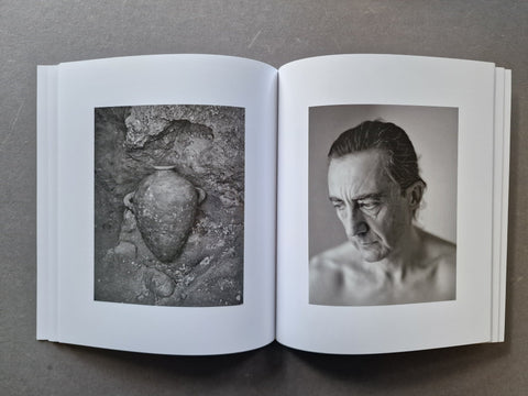 An open book, displaying two black-and-white photographic prints on the pages: a textured stone vessel on the left page and a portrait of a man on the right page.
