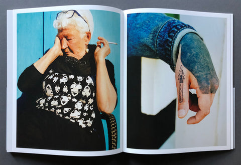 An open spread of the book toskip-a-sinking-stone by daniel-dorsa showing two printed photographs side by side: one of an elderly woman in a black top with a white skull pattern against a blue background, and another of a tattooed hand with a cigarette. The book pages are photographed on a dark gray surface.