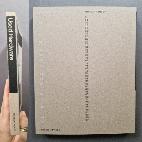 A hand holds a used copy of Martin Rinsey's 'Used Hardware' book by Harrow Press. The book has a textured, warm gray-brown cover with a black spine band on the left side displaying the title and author in white.