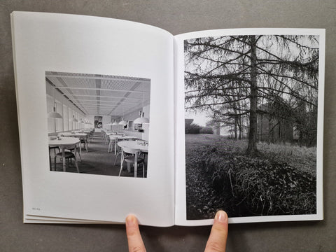 An open book showing two black-and-white photographic prints: an interior dining or exhibition space on the left page and a tree-lined outdoor scene on the right page.