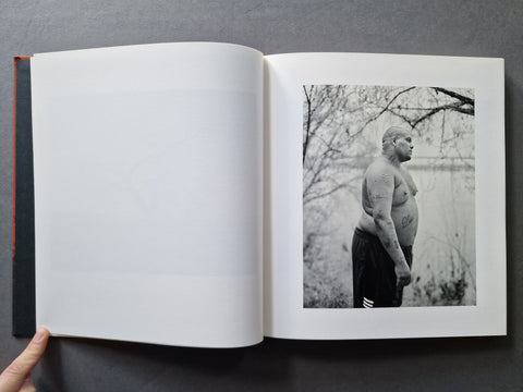 An open hardcover book with a black-and-white photograph printed on the right page showing a shirtless man standing outdoors.