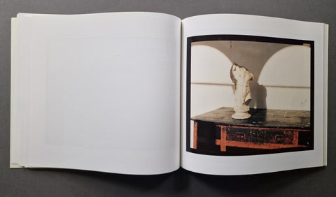 An open art book, showing a printed photograph on the right page of a white sculptural bust displayed on a dark table against a light background.