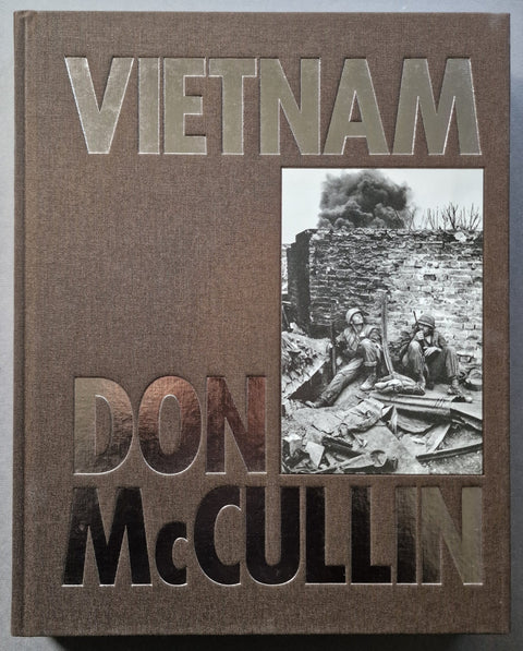 The front cover of the book 'Vietnam' by Don McCullin, featuring a textured brown cover with embossed metallic lettering and a black-and-white historical war photograph of soldiers amidst rubble.