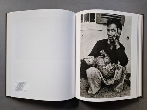 An open book, showing a black-and-white photograph printed on the right page of an open spread. The photo depicts a seated person holding a child in an outdoor setting.