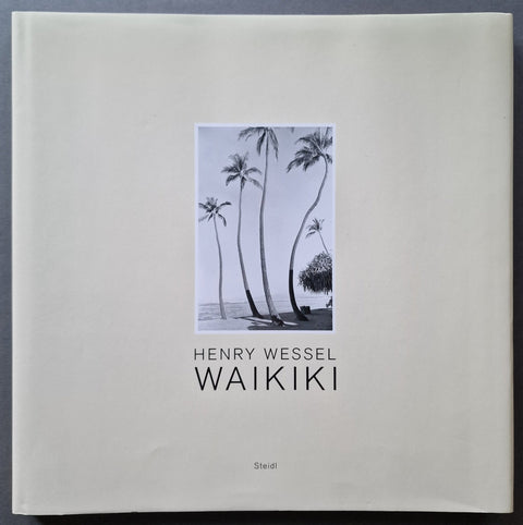 A hardcover book titled 'WAIKIKI' by Henry Wessel, featuring a minimalist off-white cover with a central black-and-white photograph of palm trees and the title printed below.