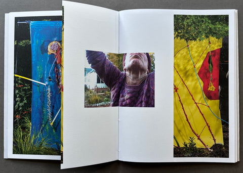 An open art book or photo journal laid flat on a dark surface, showing three printed photographs spread across the pages: a blue abstract scene on the left, a central portrait of a person reaching upward, and a yellow outdoor scene with a red flag on the right.