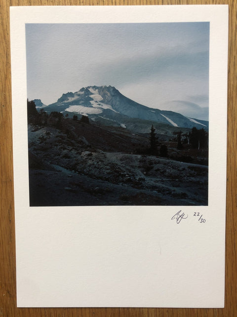 The print for photography book Between Two Mysteries by Carl Bigmore. Paperback book in blue, print image of mountain. Signed.