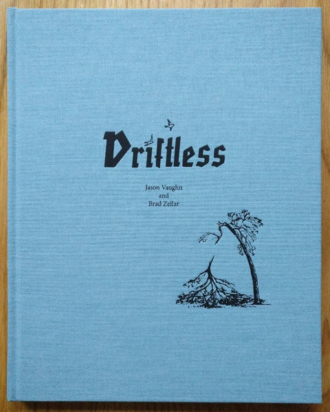 The photography book cover of Driftless by Jason Vaughn and Brad Zellar. Hardback in blue with small drawing of a broken tree on the cover.