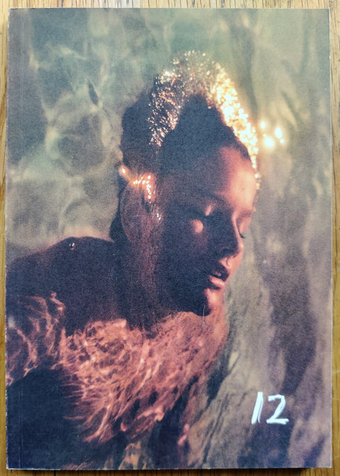 The photography book cover of 12 by Hollie Fernando. Paperback with image of a person floating in the water.