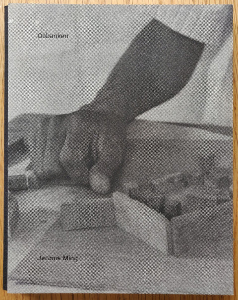 The photography book cover of Oobanken by Jerome Ming. Hardback in B&W with pixelated image.