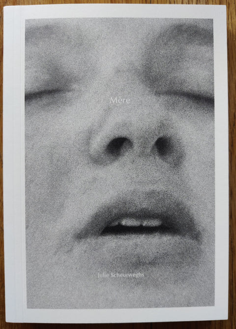 The photography boook cover of MÈRE by Julie Scheurweghs. In softcover white with a black and white close up of a face.