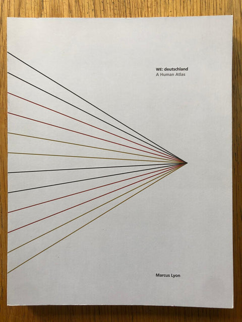 The photography book cover of WE:Deutschland by Marcus Lyon. Paperback in white with coloured diagonal lines coming to a point.