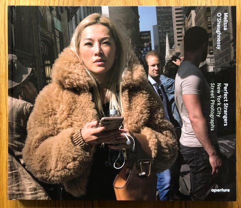 The photography book cover of Perfect Strangers: New York City Street Photographs by Melissa O'Shaughnessy. Hardback photograph of a woman in a brown fur coat on her phone.