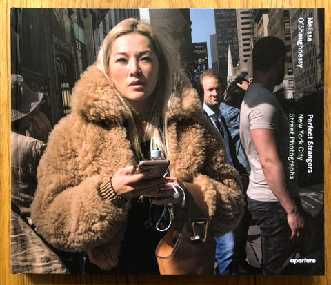 The photography book cover of Perfect Strangers: New York City Street Photographs by Melissa O'Shaughnessy. Hardback photograph of a woman in a brown fur coat on her phone.