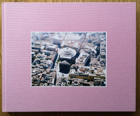 The photography book cover of ROMA - Olivo Barbieri, site specific 04-14 by Olivo Barbieri. Hardback in pink with centered aerial photo of a city. Signed.
