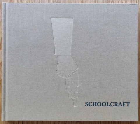 The photography book cover of Schoolcraft by Alice Schoolcraft. Hardback in grey with imprint of a hand holding a gun downwards.