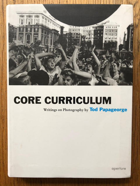 The photography book cover of Core Curriculum: Writings on Photography by Tod Papageorge. Hardback in white with B&W photo of a crowd of people with their hands up.