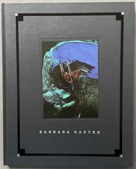 A hardcover art book titled 'Barbara Kasten' by Barbara Kasten, featuring a dark gray cover with a central abstract image of a hand holding a paintbrush, photographed against a neutral gray background.
