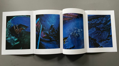 An open art book or magazine laid flat on a gray surface, showing four interior spreads with abstract blue-toned photographic prints. 