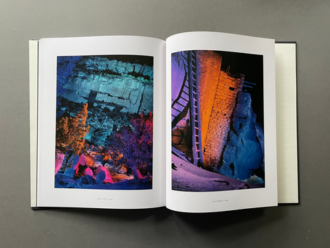 An open hardcover art book displayed flat on a dark gray surface, showing two interior pages with vibrant, colorful abstract landscape photographs.