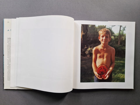 An open book, showing a large blank white page on the left and a printed photograph on the right of a shirtless boy holding a bowl of berries.