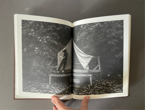 Double paged black and white image of a person building a tent. 