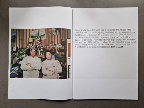 An open publication spread laid flat on a dark surface, showing a printed photograph of two men on the left page and a block of text on the right page.