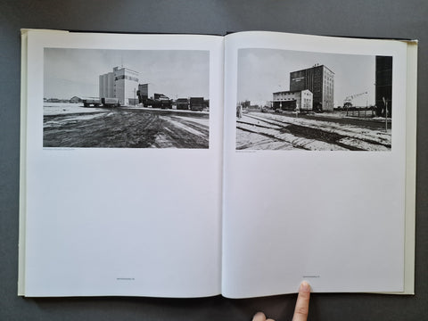 An open book showing two black-and-white architectural photographs printed on the pages, photographed from above on a dark gray surface. 