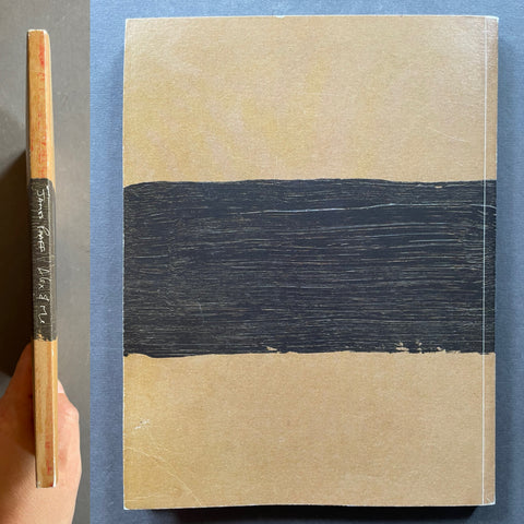 A square art book or notebook with a minimalist cover design, shown from the front and side. The cover is a warm beige/tan color with a wide horizontal black brushstroke across the center.