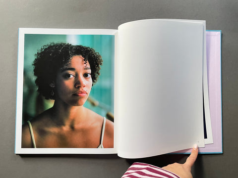 An open hardcover art book or photo journal lying on a dark gray surface. The left page shows a printed portrait photograph of a woman with curly hair, and the right page is blank white.