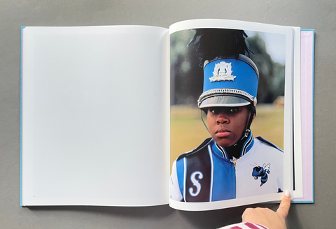 An open hardcover photo book or album lying on a gray surface, showing a printed portrait of a person in a blue and white marching band uniform on the right page. 