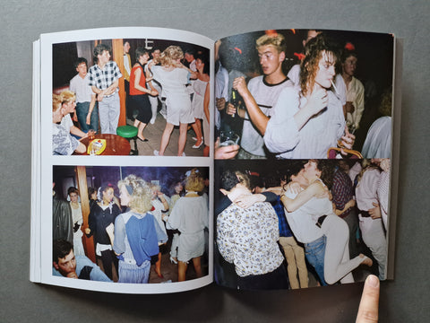 An open photobook showing four vintage-style party and social scene photographs printed on the pages, photographed against a dark gray background with a finger visible at the bottom right.