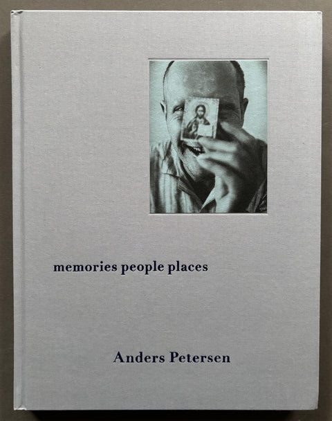Book titled 'Memories People Places' by Anders Petersen with a grey cover featuring the photograph of a man holding a small image of Jesus in front of his face.