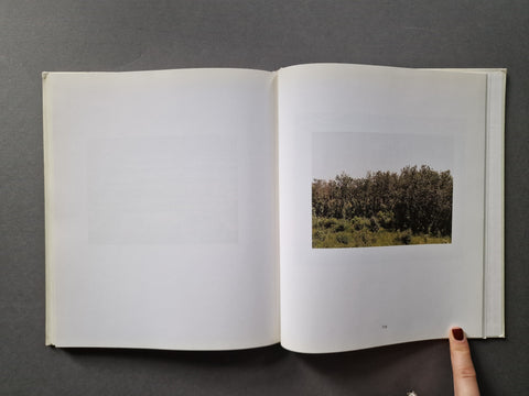 An open book, showing mostly blank white pages on the left and a small landscape photograph of trees on the right. 