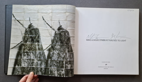An open book  showing a black-and-white photograph of two moths on the left page and a signed title page on the right.