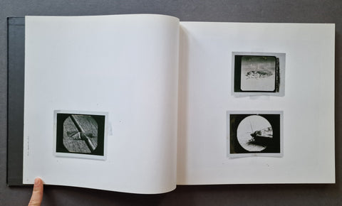 An open book spread on a dark gray surface, showing two black-and-white photographs of moths on the right page and one on the left.