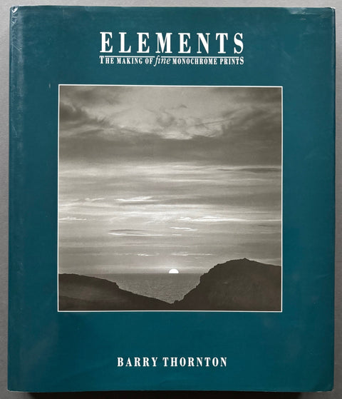 Book titled 'Elements: The Making of Fine Monochrome Prints' by Barry Thornton with a blue cover featuring the black and white image of a sun rising over the sea with a cloudy sky.