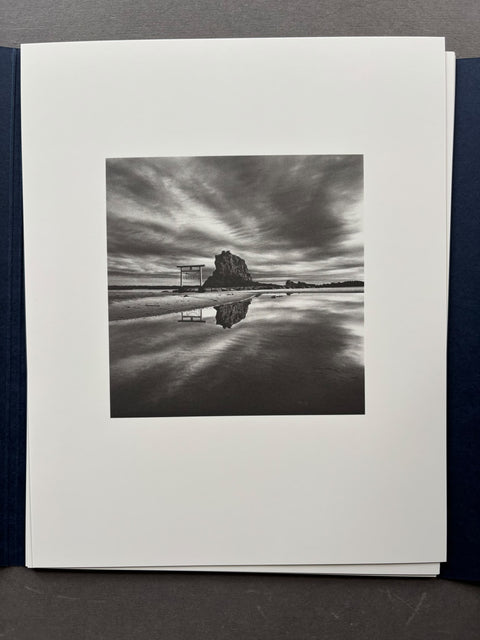 A black and white landscape photograph of a sea landscape and a rock in the distance